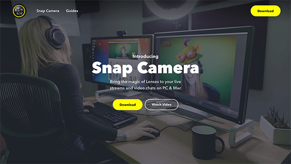 Esta é uma captura de tela do site Snap Camera. No fundo da página, uma mulher está sentada em um computador desktop com fones de ouvido, usando lentes de realidade aumentada para fazer parecer que ela está usando um chapéu bobo de desenho animado. O texto em branco no centro da página diz “Traga a magia do Lenses para suas transmissões ao vivo e chats de vídeo no PC e Mac”. Um botão amarelo é denominado Download.